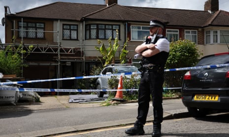 Police stand outside the home of a man arrested for a sword attack in Hainault, east London.