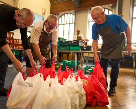 Three men bending over an ordered collection of white and red plastic food bags