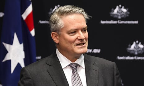 grey haired man in dark suit with white shirt and tie and australian flag in background
