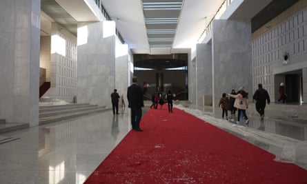 People inside the presidential palace in a hall with a red carpet covered in debris