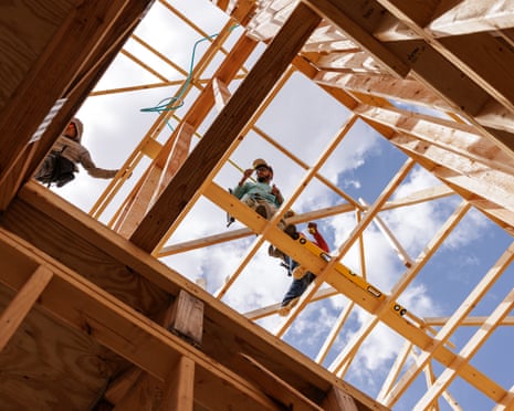 a view from the ground looking up towards constructions workers as they work on the wooden framing of what will become a townhouse