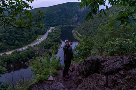 A man takes a selfie on a trail, a highway in the background