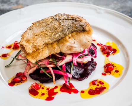 A pice of fish is perched on top of a colourful pile of beetroot, cabbage and cavolo nero and surrounded by bright blobs of oil and pomegranate seeds.