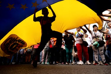A person in silhouette dancing under a large Venezuelan flag that is being waved over the ground