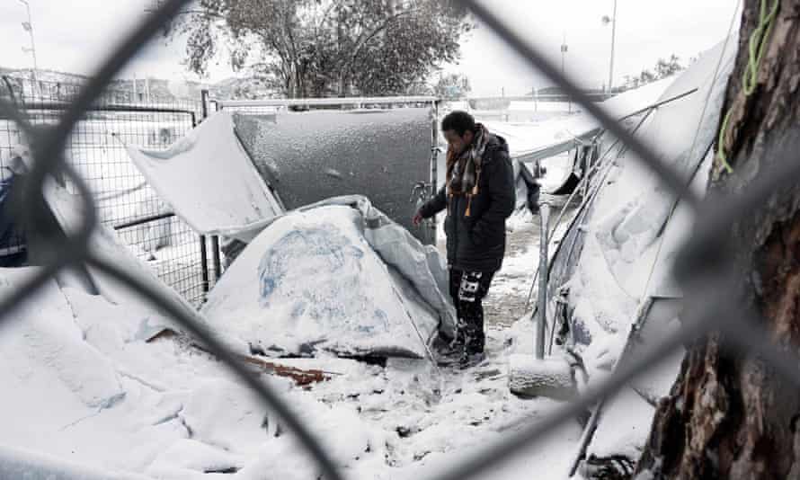 A man stands next to a snow-covered tent in the Moria camp on the island of Lesbos.
