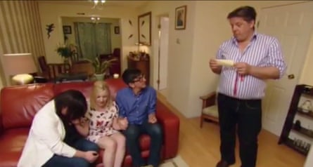 Man stands to read out winner to his fellow contestants sitting on the sofa