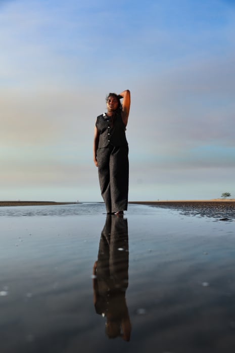 A woman wearing a dark outfit walks along a beach