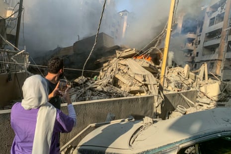 A woman takes photos with her phone of the destruction caused by an Israeli airstrike on Beirut.