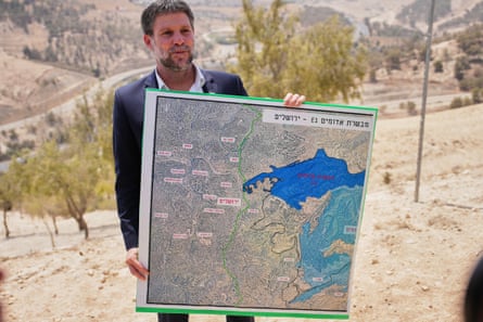 Man in beard with suit in arid landscape with map featuring areas marked out in blue.