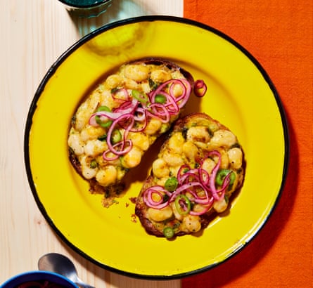A yellow plate with two slices of toast topped with cheesy curried butter beans and pickled onions.
