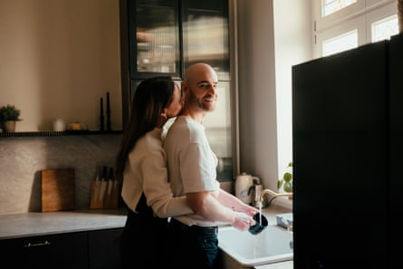 A couple kiss and the man washes dishes.