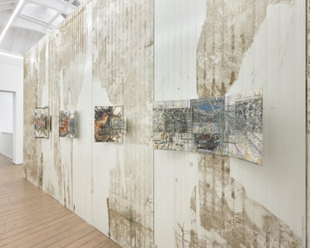 A row of metal collages are displayed on rusting, filthy walls