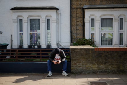 A lone Spurs fan looks at his phone as he sits on a wall on Park Lane near the stadium