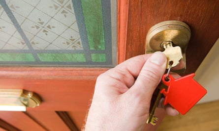 Someone opening a front door with a key on a house-shaped keyring