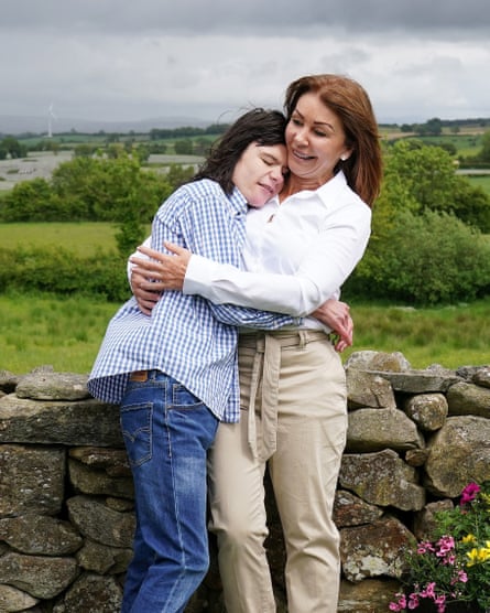 Charlotte hugs Billy beside a dry stone wall with a rural scene in the background.