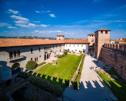 Medieval buildings and towers around a courtyard against a blue sky.