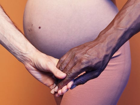 The hands of a black man and a white man touching in front of the pregnant belly of a white woman