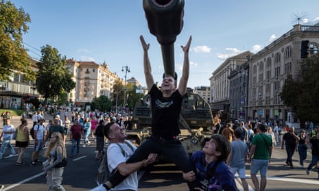 Two smiling men lift up a third who raises his arms towards the barrel of an artillery vehicle