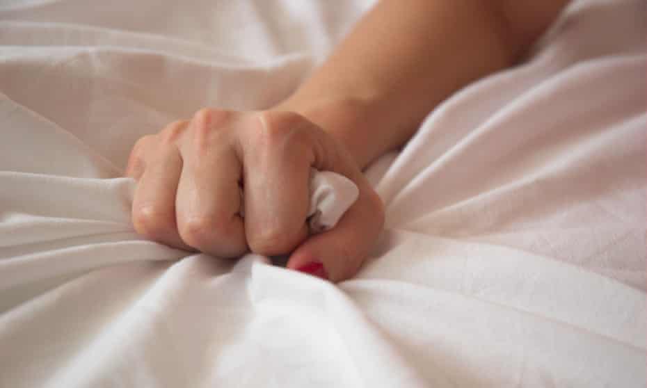 A woman's hand squeezing a bed sheet