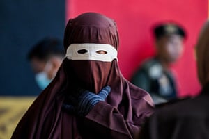 A close-up of person covered head-to-toe in a maroon cloak and hood and wearing a white eye mask