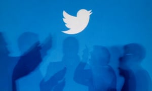 Shadows of people holding mobile phones are cast onto a backdrop projected with the Twitter logo