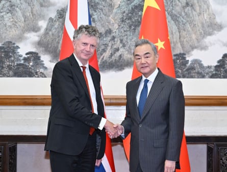 two men shaking hands in front of a UK flag and a Chinese flag