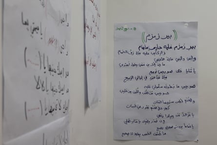 Large pieces of paper with song lyrics in Arabic hang on a wall.