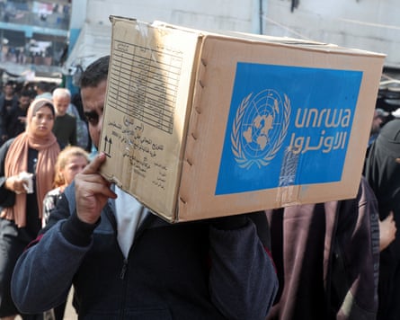A man carries a cardboard box marked with the logo of Unrwa.