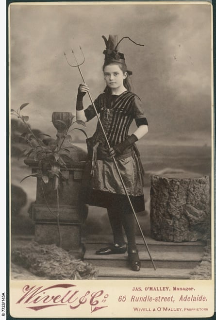 A young girl wearing a dark costume holding a pitchfork