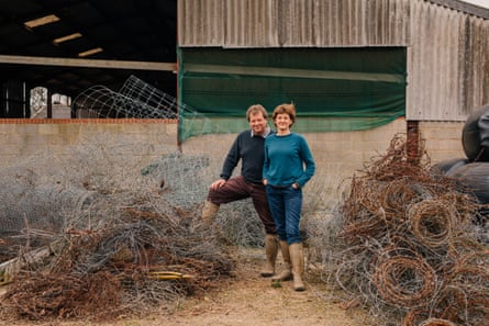 A couple stand in a farmyard amid a pile of rusting wire fencing