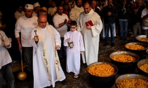 Priests in robes blessing large vats of pasta.