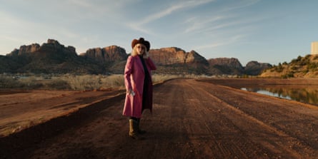 a woman stands outdoors against a background of mountains