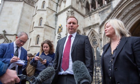Tom Hayes in a suit and tie stands with his hands in his pockets, surrounded by reporters and microphones, outside the entrance tot he Royal Courts of Justice