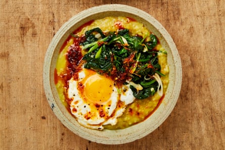 Closeup of a bowl of freek and oat porridge flavoured with turmeric, and topped with a fried egg, wilted garlicky spinach and ginger oil.