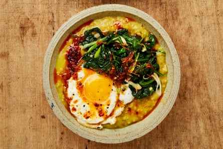 Close-up of a bowl of freek and oatmeal porridge flavored with turmeric, topped with a fried egg, wilted garlic spinach and oil of ginger.