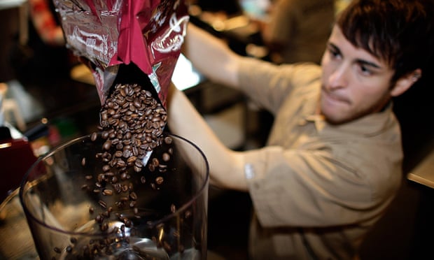 An employee pours coffee beans into a grinder at a Costa Coffee shop in London