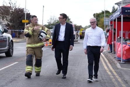 Andy Burnham and Richard Parker walk with Simon Tuhill in his full firefighter uniform