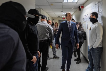 a man in a suit walks past masked federal agents