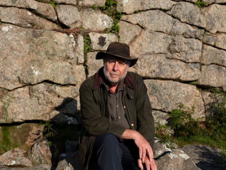 A man in a back hat sits in front of a rock formation.
