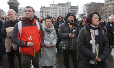 People stand holding white flowers in Trafalgar Square