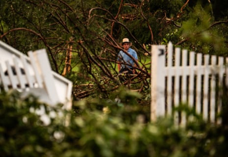 a man looks at downed trees by white picket fence