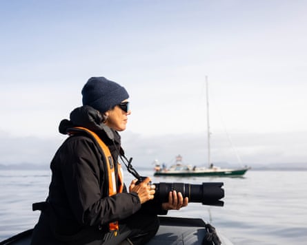 A woman on a small boat with a long lens camera looking at something at sea