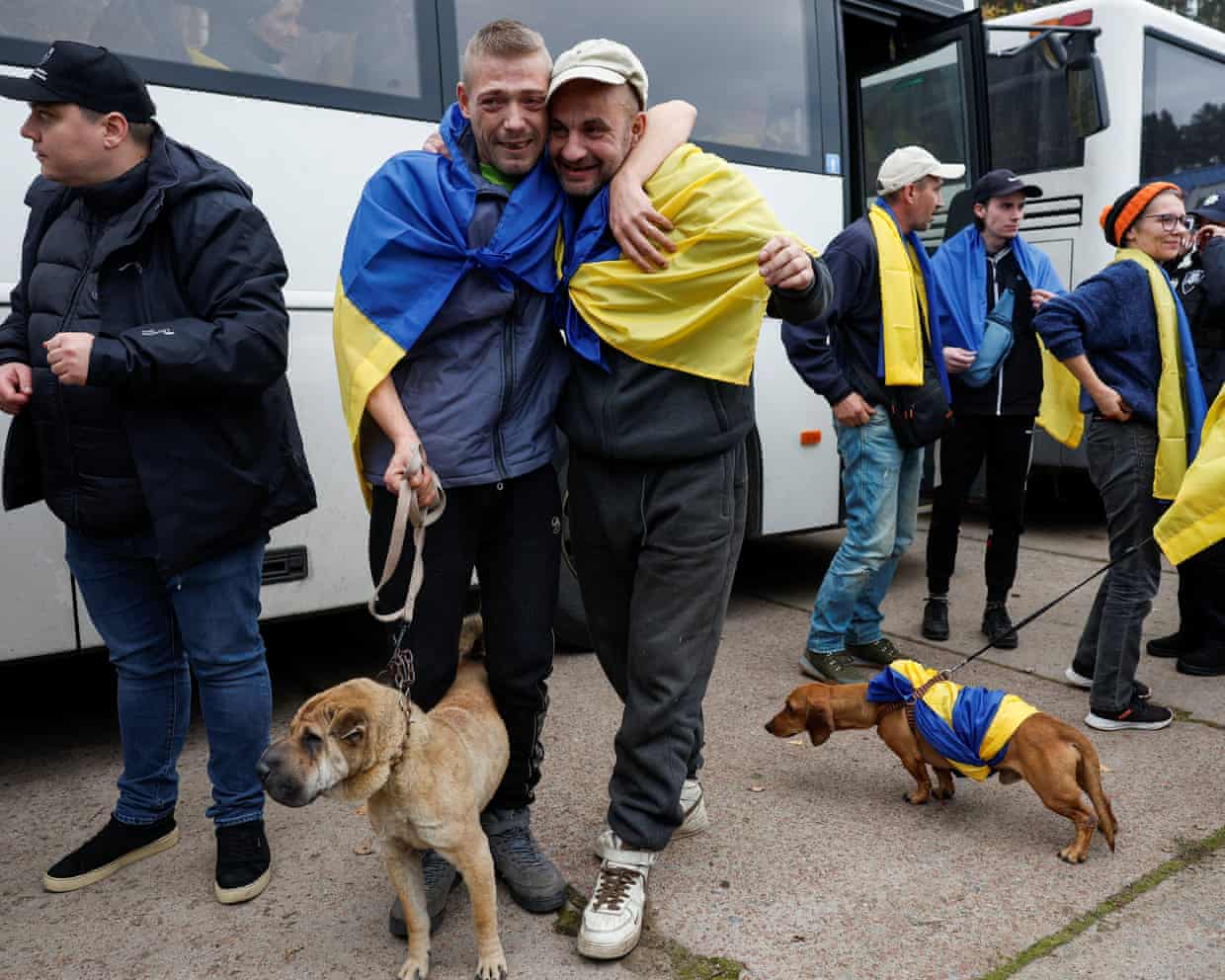 Evacuated residents embrace tearfully in Ukrainian flags, with dogs beside them near a bus