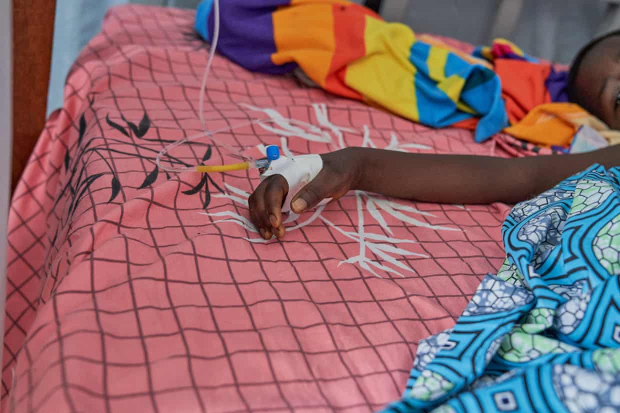 A patient lies in bed with a cannula in their hand.