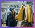A woman in a beanie and glasses examines a yellow jacket on a clothing rack