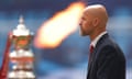 Erik ten Hag walks on to the pitch, with the FA Cup trophy and pyrotechnics in the background.