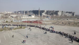 People stand in a long queue during the distribution of humanitarian aid near damaged blocks of flats in the besieged southern port city of Mariupol.