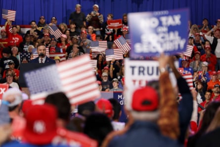 People holding Trump signs in front of a man at a lectern