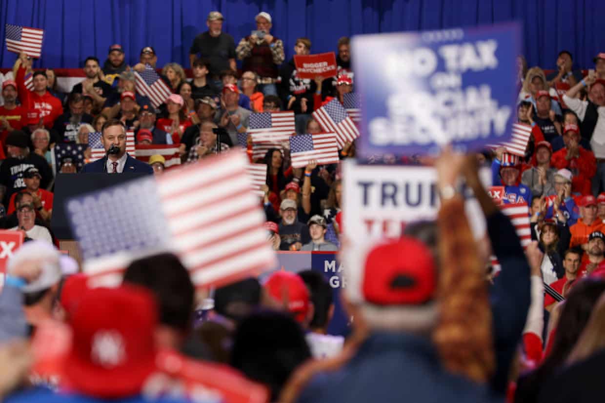 People holding Trump signs in front of a man at a lectern