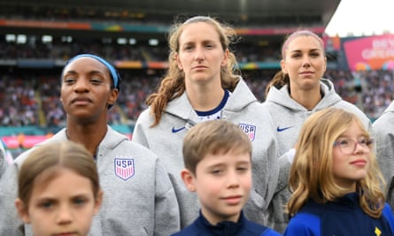 Naomi Girma, Andi Sullivan and Alex Morgan, in USA sweatshirts, stand unsmiling waiting for the national anthem